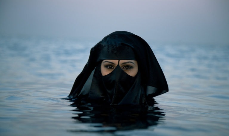 Cette photo montre une femme dans l'eau jusqu'au cou. Elle porte sur la tête un voile et un niqab dissimule son visage. Son exemple illustre ce que les auteurs de cet article considère comme une atteinte à la dignité de la femme.