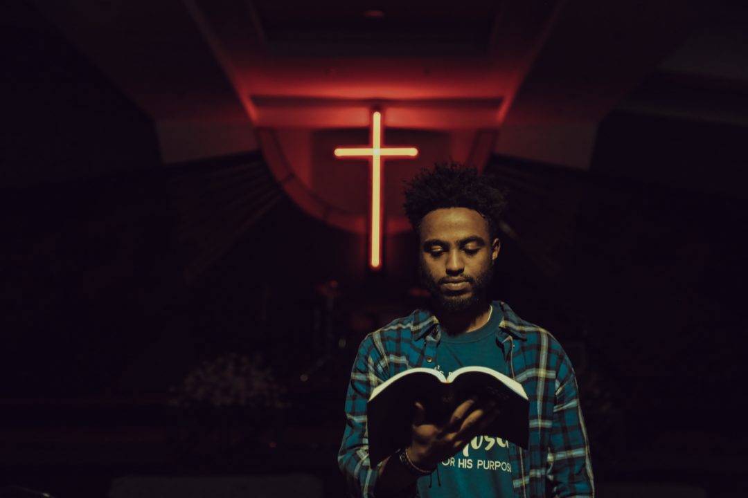 Cette photo représente un chrétien lisant la Bible devant une croix.