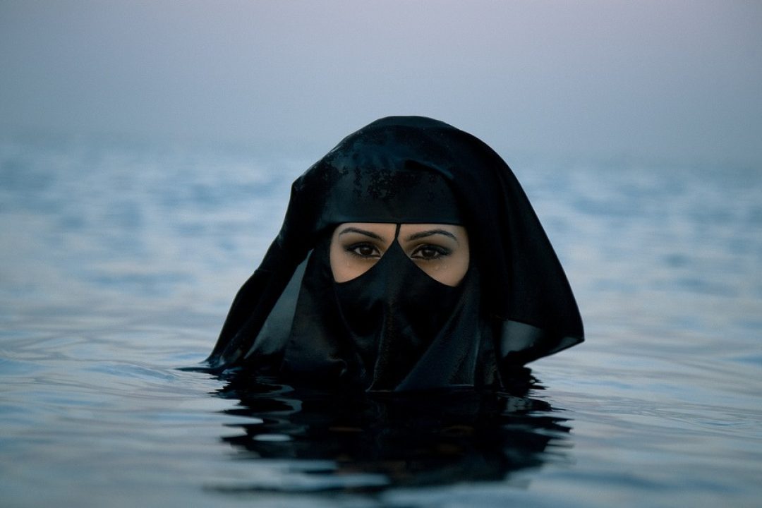 Cette photo montre une femme dans l'eau jusqu'au cou. Elle porte sur la tête un voile et un niqab dissimule son visage. Son exemple illustre ce que les auteurs de cet article considère comme une atteinte à la dignité de la femme.